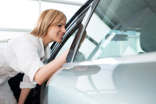 Mid adult woman looking through a opened window of a car in a showroom.