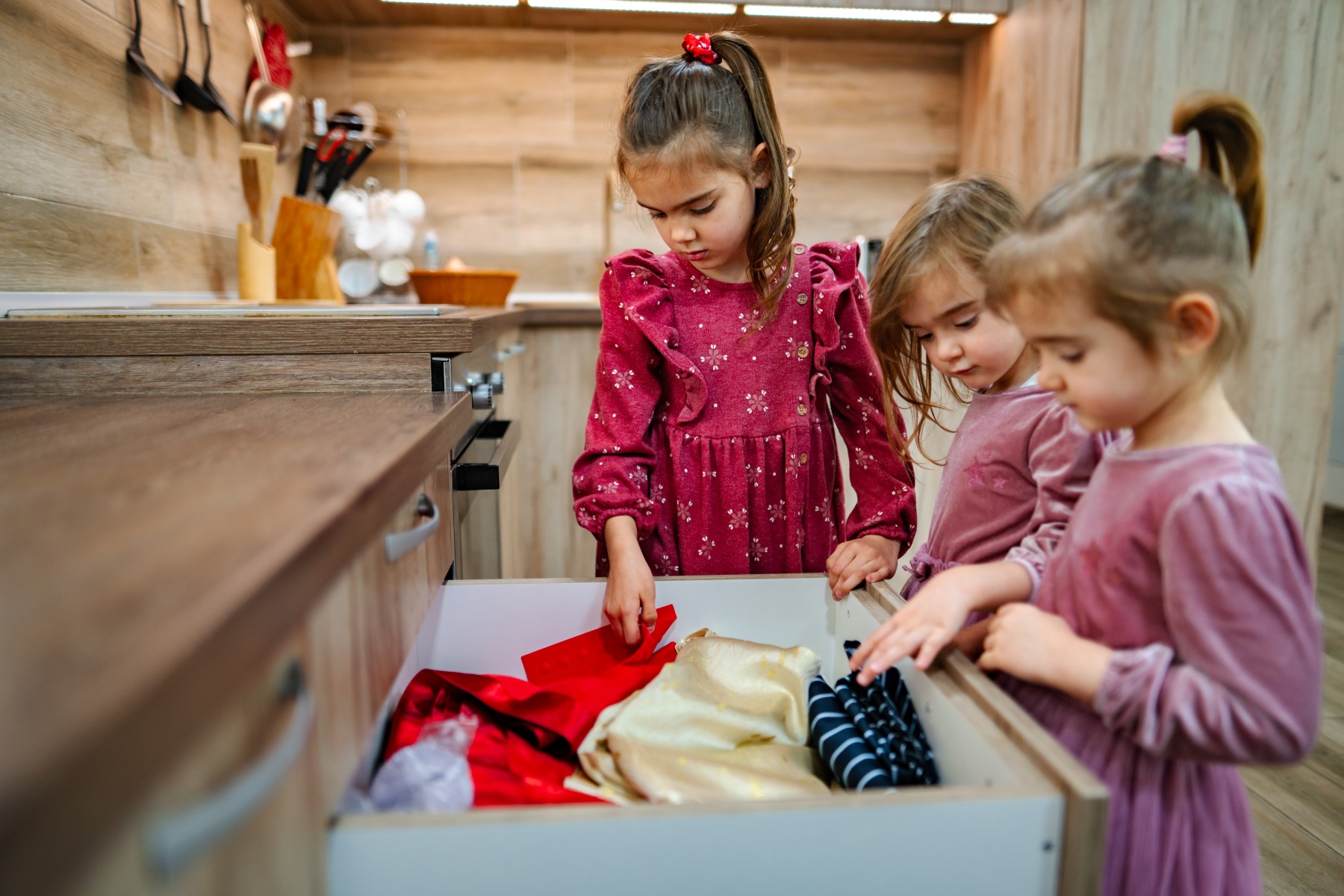 Three girls exploring a kitchen drawer full of costumes